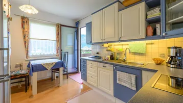 Funktionale Küche mit blauen und weißen Schränken, Essbereich und Zugang zum Balkon.