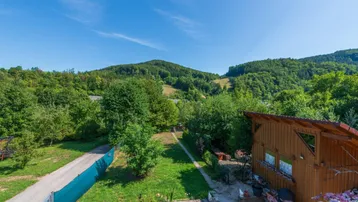 Panoramablick über die grüne Hügellandschaft mit Bäumen und einem kleinen Nebengebäude.