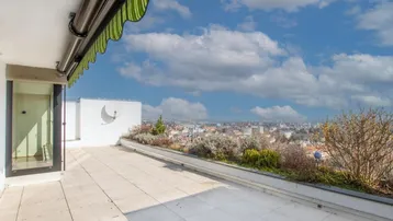 Helle Terrasse mit Markise und Panoramablick über die Stadt und die grüne Umgebung.