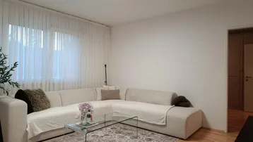 Helles Wohnzimmer mit beigem Ecksofa, Holzboden und einem modernen Deckenlicht.
