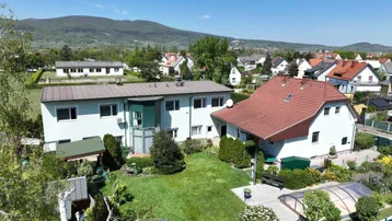Luftaufnahme zweier Häuser mit großem Garten und Blick auf die umliegende Landschaft und Berge.