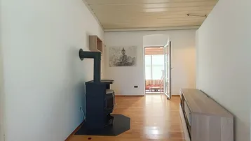 Wohnzimmer mit Holzboden, Kaminofen und Zugang zu einem Balkon oder Wintergarten.