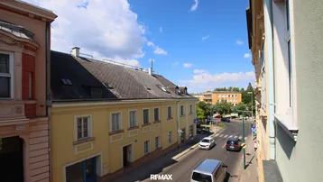 Blick von oben auf eine belebte Straße mit historischen Gebäuden unter blauem Himmel.