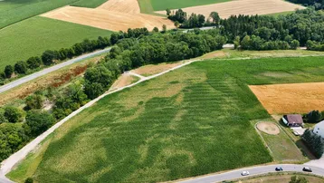 Luftaufnahme einer ländlichen Gegend mit Feldern, Wäldern und einer Straße, die sich durch die Landschaft schlängelt.