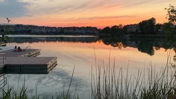 Malerischer Sonnenuntergang über einem ruhigen See mit Steg und üppiger Ufervegetation.