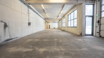 Großer, leerer Gewerberaum mit Betonboden, hohen Decken und großen Fenstern, ideal für Lager oder Produktion.