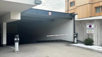Einfahrt zur Tiefgarage mit Schranke und Höhenbegrenzung, umgeben von moderner Architektur.