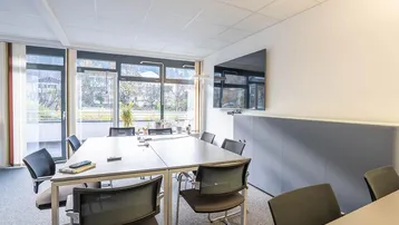 Heller Konferenzraum mit großem Tisch, modernen Stühlen und Blick ins Grüne durch bodentiefe Fenster.