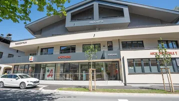 Modernes Geschäftsgebäude mit Apotheke und Arztpraxen im Erdgeschoss, umgeben von Bäumen.