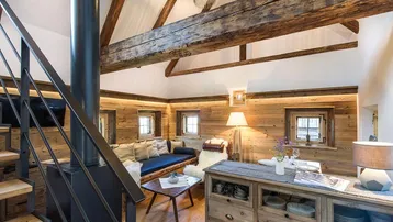 Gemütliches Wohnzimmer im alpinen Stil mit sichtbaren Holzbalken und modernem Kaminofen.