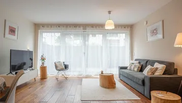 Helles Wohnzimmer mit Holzboden, bequemer Couch und großen Fenstern, die viel Tageslicht hereinlassen.
