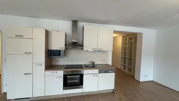 Moderne Küchenzeile in einem offenen Wohnbereich mit integrierten Geräten und Blick auf ein Regal.