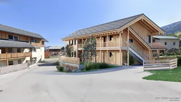 Modernes Holzgebäude mit mehreren Balkonen und Außentreppe in alpiner Umgebung, umgeben von Natur.