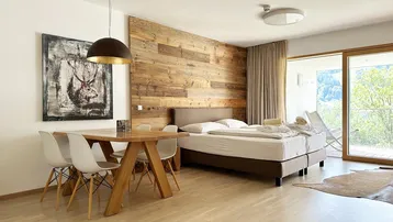 Helles Schlafzimmer mit Holzwand, Essbereich und Zugang zum Balkon mit Bergblick.