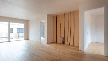 Heller, unmöblierter Wohnbereich mit Holzboden und Zugang zum Balkon, bereit für den Innenausbau.