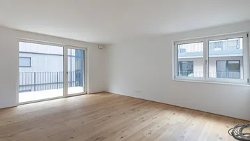 Heller, leerer Raum mit modernem Holzfußboden und großem Fenster mit Balkonzugang.