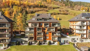 Moderne Apartmentgebäude in alpiner Landschaft mit herbstlicher Vegetation und Bergblick.