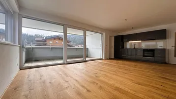 Helles, offenes Wohnzimmer mit integrierter Küche, Holzboden und Zugang zum Balkon mit Bergblick.