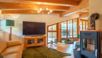 Gemütliches Wohnzimmer mit Kaminofen, Ledersofa und großen Fenstern mit Bergblick.