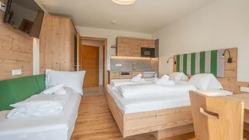 Gemütliches Schlafzimmer mit Holzboden, Doppelbett, Einzelbett und integrierter Küchenzeile.