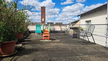 Geräumige Dachterrasse mit Pflanzen, Sitzgelegenheiten und Blick auf die Umgebung unter blauem Himmel.