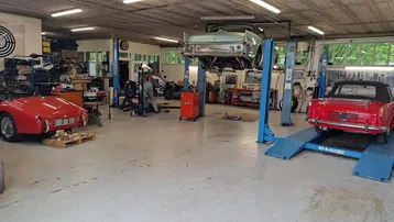 Geräumige Werkstatt mit Hebebühnen und klassischen Fahrzeugen, ideal für Oldtimer-Reparaturen und Wartung.