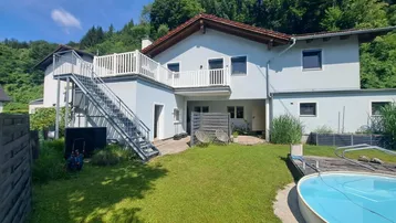 Hinteransicht des Hauses mit Garten, oberirdischem Pool und Außentreppe zur oberen Terrasse.