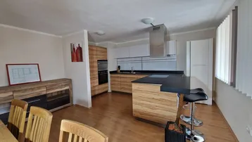 Moderne offene Küche mit Holzelementen, dunkler Arbeitsplatte und integrierten Geräten in einem hellen Raum.