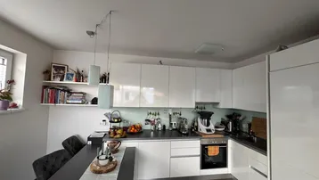 Moderne Küche mit weißen Hochglanzfronten, dunkler Arbeitsplatte und integriertem Backofen.
