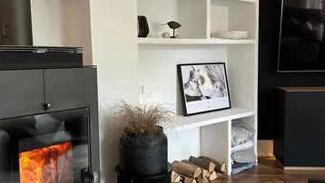 Gemütliches Wohnzimmer mit modernem Kaminofen, Holzregal und dunklem Laminatboden.