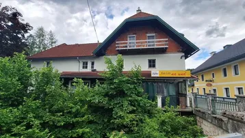 Ansicht des Gebäudes mit traditioneller Architektur, umgeben von üppigem Grün und Bäumen.