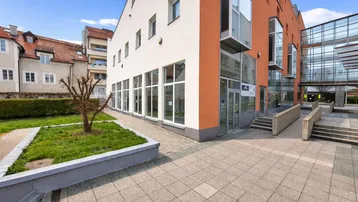 Moderne Architektur mit weißer und oranger Fassade, großen Fenstern und gepflastertem Vorplatz.