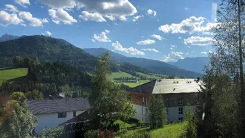 Idyllisches Haus in grüner Hügellandschaft mit beeindruckendem Bergblick unter blauem Himmel.