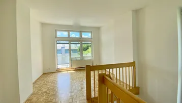 Lichtdurchfluteter Wohnbereich mit Parkettboden, Holztreppe und Blick ins Grüne.