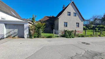 Einfamilienhaus mit Satteldach und angrenzender Garage in ländlicher Umgebung.