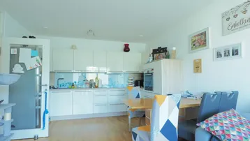 Helle offene Küche mit weißen Schränken und Essbereich, integriert in den Wohnraum mit Holzboden.