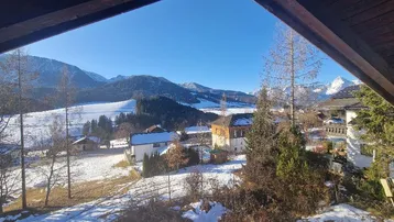 Winterliche Aussicht auf schneebedeckte Landschaft mit Häusern und Bergen unter strahlend blauem Himmel.