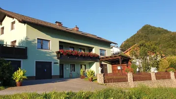 Hausfassade in hellem Grün mit Balkonen und Bergblick in ländlicher Umgebung.