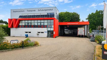 Modernes Geschäftsgebäude mit großen Fenstern, Solarpaneelen auf dem Dach und einem Industriebereich.