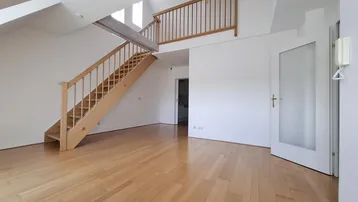 Helles Wohnzimmer mit Holztreppe, Parkettboden und hohen Decken, das zu einer Galerie führt.