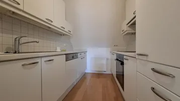 Funktionale Küche mit weißen Einbauschränken, Fliesenrückwand und integrierten Geräten unter der Dachschräge.