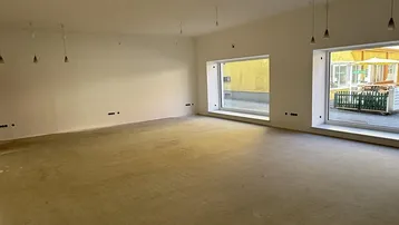 Großer, leerer Raum mit großen Fenstern und unfertigem Boden, bereit für den Ausbau.