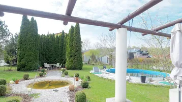 Gepflegter Gartenbereich mit Pool, Kieswegen und einer gemütlichen Sitzecke unter einer Pergola.