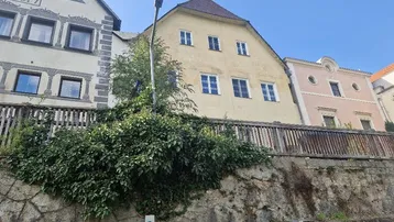 Verschiedene historische Gebäude mit unterschiedlichen Fassaden und einem bewachsenen Mauersockel.