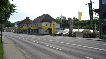 Außenansicht eines Autohauses mit Ausstellungsflächen und Parkplätzen entlang einer Straße.