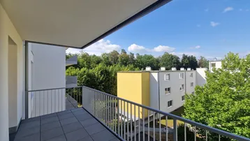 Geräumiger Balkon mit Fliesenboden und Blick ins Grüne sowie auf umliegende Gebäude.