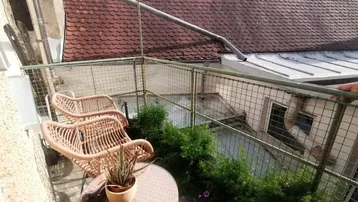 Kleiner Balkon mit Korbmöbeln und Pflanzen, mit Blick auf ein rotes Ziegeldach.