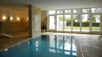 Großzügiger Innenpoolbereich mit großen Fenstern und Blick ins Grüne.