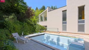 Modernes Haus mit großen Fenstern und einem gepflegten Außenpoolbereich im Grünen.