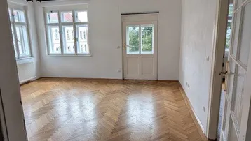 Helles Wohnzimmer mit Fischgrätparkettboden, hohen Decken und großen Fenstern, typisch für einen Altbau.